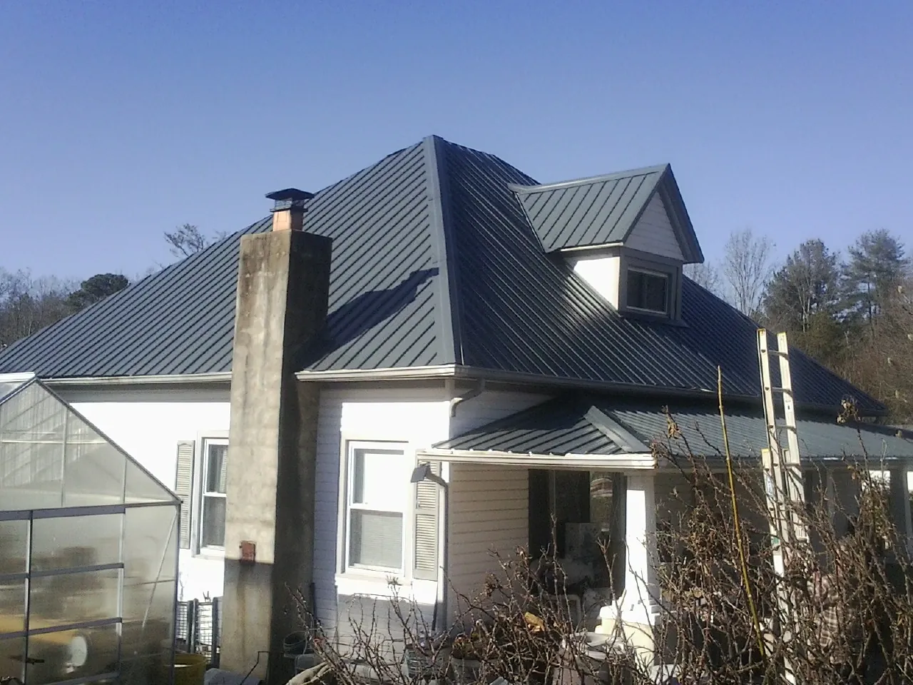 Dark blue standing seam metal roof on a white farmhouse with dormer — Slate & Tile Roof Repair by Roofing Brothers in Preble