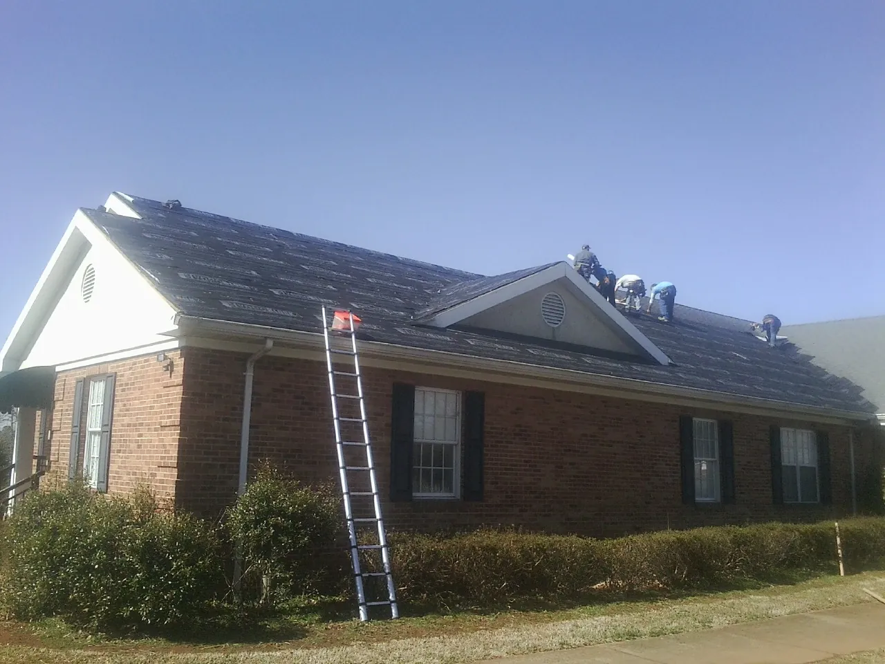 Crew tearing shingles off a brick ranch roof with a ladder set — Emergency Roof Repair work by our crew in Preble