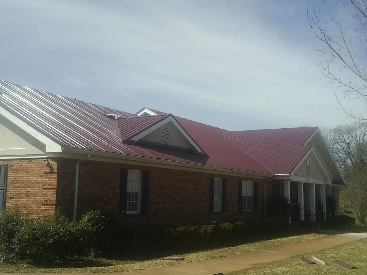 Red metal roof with gabled entries on a long brick building, from a Hail Damage Roof Repair job in Preble