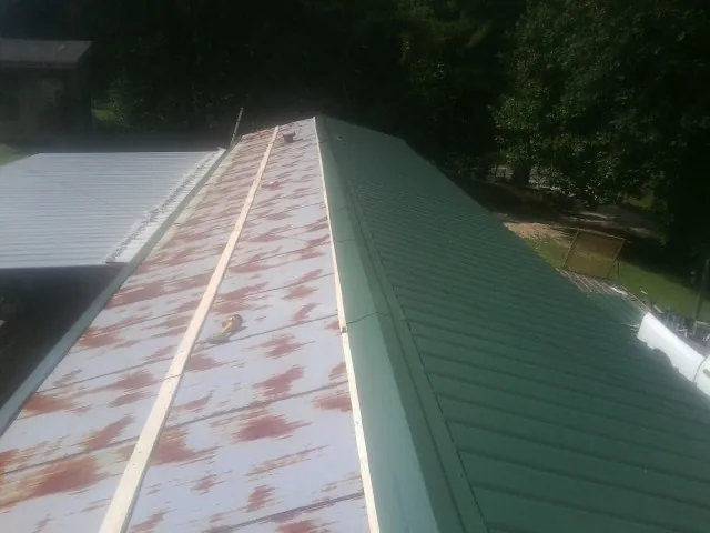 Old rusted panels beside newly installed green metal roofing — Wind Damage Roof Repair by Roofing Brothers in Preble