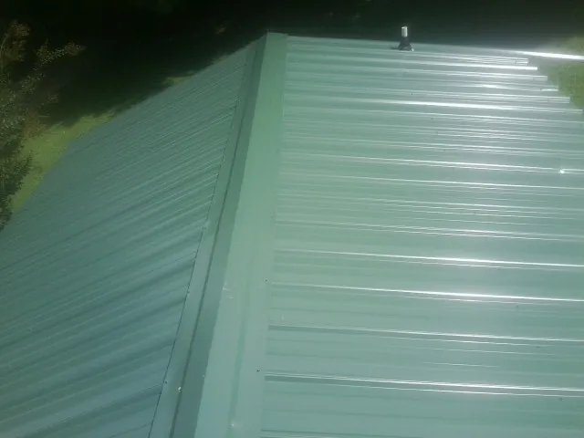 New green metal panels meeting at the ridge of a roof — Flat Roof Repair work by our crew in Preble