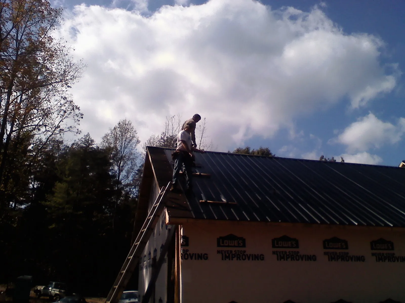 Roofer fastening dark metal panels high against a cloudy sky, from a Roof Inspection job in Preble